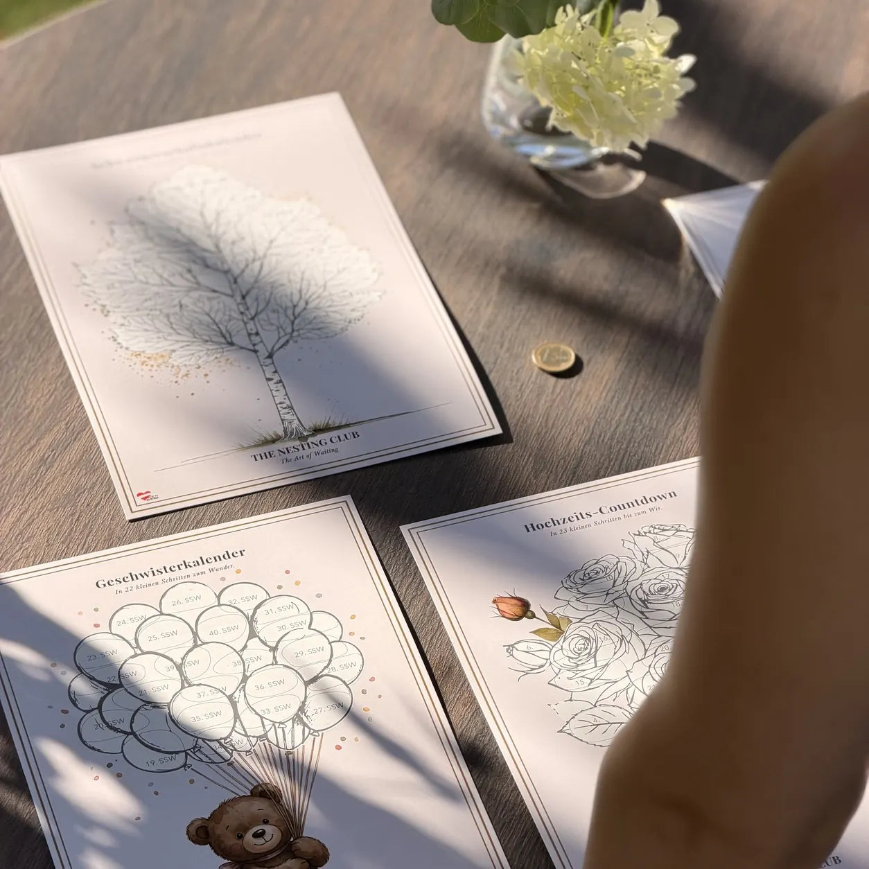 Mehrere Rubbelkalender von The Nesting Club auf einem Gartentisch – echtes Foto